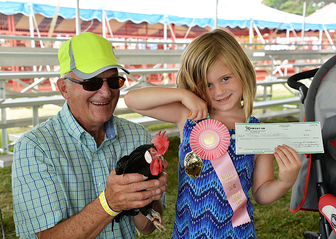 a girl and her grandpa show off their rooster, ribbon and check from the Carver County Fair rooster crowing contest