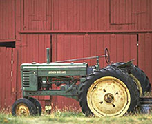 a green tractor parked in front of a red barn