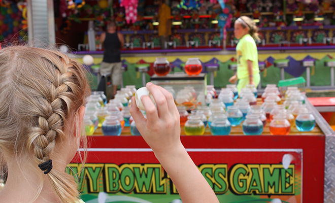 a girl with pigtails prepares to throw a ball in a carnival game at the Carver County Fair midway