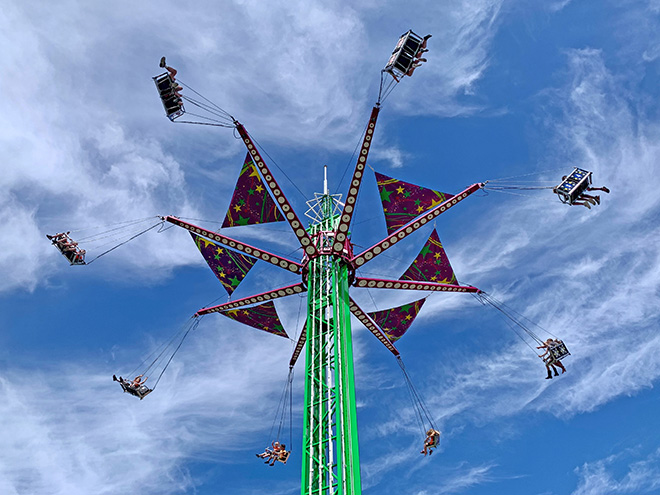 people ride in swings in a Carver County Fair Midway ride silhouetted against the sky