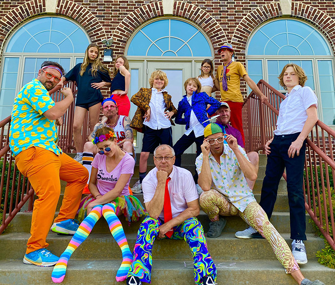 The Dweebs promo photo: a dozen people including children pose on the steps of a building