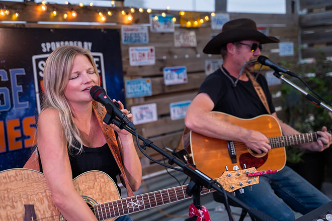 a woman sings while a man plays a harmonica and strums an acoustic guitar