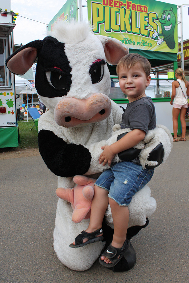 Tippy the Cow mascot poses with a little boy on her knee